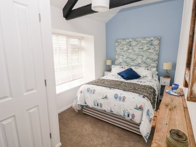 A bedroom with a bed bedside tables lamps and a wooden shelf at Bluebell Cottage in Jameston near Manorbier