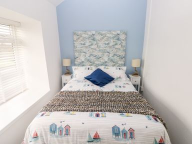 A bedroom with a bed with a patterned headboard and bedding with seaside designs at Bluebell Cottage in Jameston near Manorbier