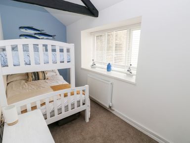 A small bedroom with white bunk beds next to a window with blinds and decorative items on the sill at Bluebell Cottage Jameston near Manorbier