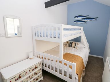 A bedroom with a white bunk bed a small white chest of drawers with nautical designs a mirror on the wall and fish decoration on a blue wall at Bluebell Cottage Jameston near Manorbier