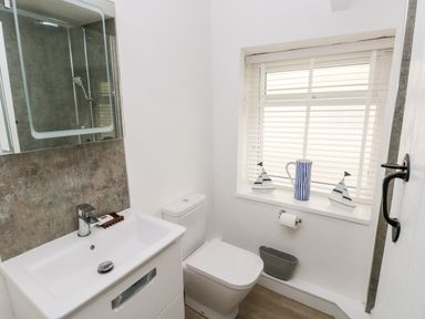 A bathroom with a sink, toilet, window with blinds and decorative items at Bluebell Cottage in Jameston near Manorbier