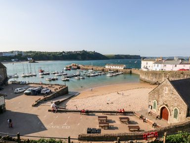 A small harbor with boats docked near a sandy beach and stone buildings at Bluebell Cottage in Jameston near Manorbier