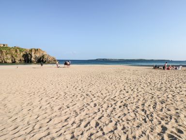 A sandy beach with groups of people near the water and rocky cliffs at Bluebell Cottage in Jameston near Manorbier