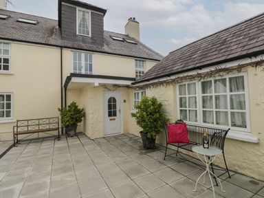 A patio area with benches plants and a small table outside a cream colored house at Bluebell Cottage in Jameston near Manorbier