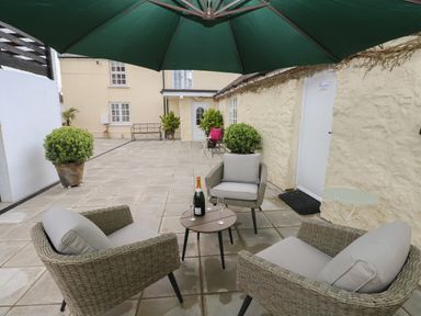 An outdoor patio with wicker chairs around a table under a green umbrella at Bluebell Cottage in Jameston near Manorbier