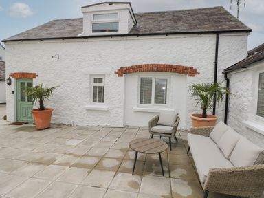 An outdoor patio with a sofa chair table and potted palm plants at Bluebell Cottage Jameston near Manorbier
