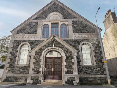 Stone facade of English Presbyterian Church with arched windows and double doors at The Church in Holyhead