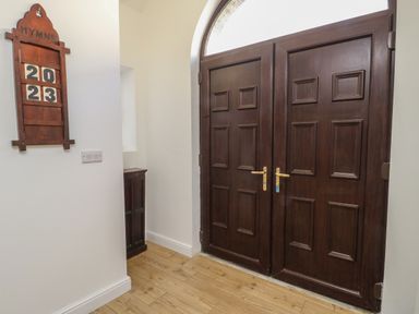 A hallway with dark wooden double doors and a wooden hymn board on a white wall at The Church in Holyhead