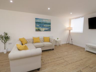 A living room with a beige sofa with yellow pillows a sea painting on the wall a floor lamp a wall-mounted television and wooden flooring at The Church in Holyhead