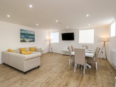 A living room with beige sofas yellow cushions a dining table with chairs wall-mounted tv and floor lamps at The Church in Holyhead