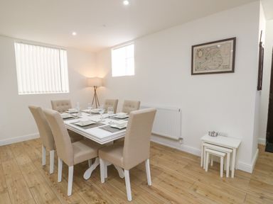 A dining room with a table set for six and beige chairs a floor lamp and a framed map on the wall at The Church in Holyhead