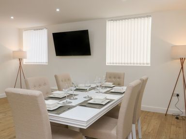 A dining room with a white table and beige chairs set with white dishes and glassware at The Church in Holyhead