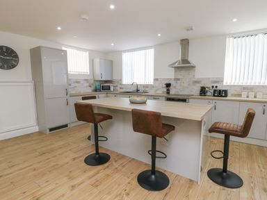 A kitchen with a central island and three brown bar stools at The Church in Holyhead