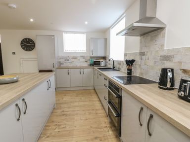 A kitchen with wooden countertops white cabinets black appliances and a wall clock at The Church in Holyhead