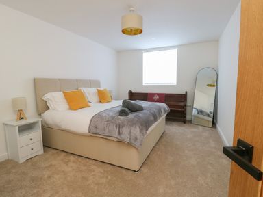 A bedroom with a bed side table and lamp a wooden bench a floor mirror and a bed with pillows and blankets at The Church in Holyhead
