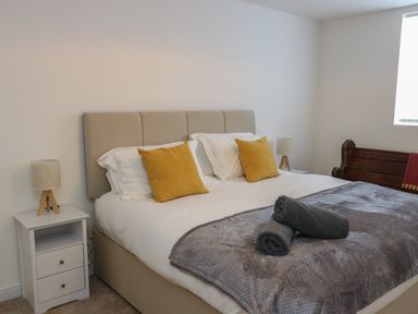 A bedroom with a bed with yellow pillows gray blanket and rolled towels flanked by bedside tables with lamps at The Church in Holyhead