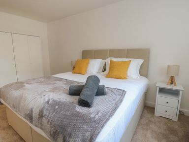 A bedroom with a bed featuring yellow pillows gray rolled towels and a bedside table with a lamp at The Church in Holyhead