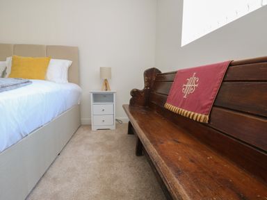 A bedroom with a bed white nightstand lamp and wooden bench with red cloth at The Church in Holyhead