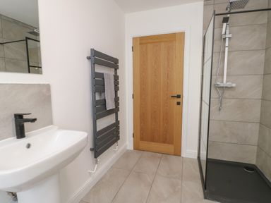 A bathroom with a sink and black faucet a towel rack a wooden door and a shower with glass panels and a rainfall showerhead at The Church in Holyhead