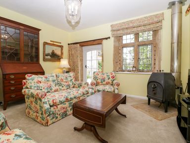 A sitting room with floral upholstered sofa and chairs wooden coffee table wood stove and cabinet at Ham cottage East Lambrook near South Petherton