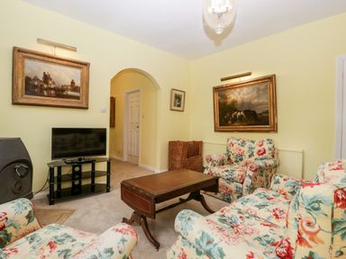 A living room with floral upholstered armchairs a television on a stand and framed paintings on yellow walls at Ham cottage East Lambrook near South Petherton