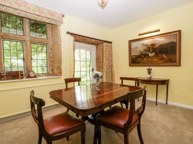 A dining room with wooden table and chairs near windows and a painting on the wall at Ham cottage in East Lambrook near South Petherton