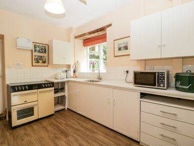 A kitchen with an oven, cabinets, a microwave, a bread bin, and a window with a red blind at Ham cottage East Lambrook near South Petherton