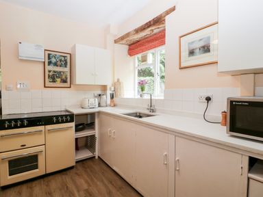 A kitchen with a stove toaster kettle knives cutting boards microwave and a window with flowers at Ham cottage in East Lambrook near South Petherton
