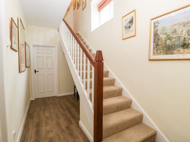 A hallway with carpeted stairs wooden handrail framed pictures and a closed white door at Ham cottage in East Lambrook near South Petherton