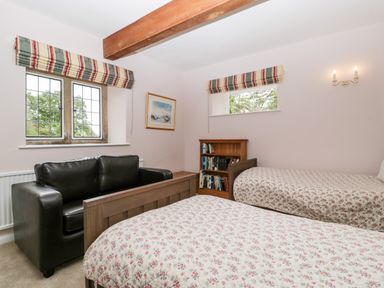 A bedroom with two single beds covered in floral bedspreads a black leather armchair a wooden bookshelf and two windows with striped blinds at Ham cottage East Lambrook near South Petherton