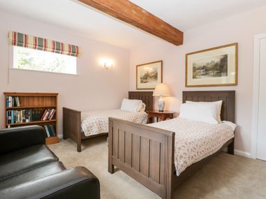 A bedroom with two single beds a wooden bookshelf and a black armchair at Ham cottage in East Lambrook near South Petherton