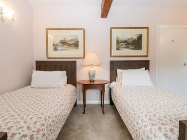 A bedroom with two single beds with floral bedspreads a wooden bedside table with a lamp and two framed pictures on the wall at Ham cottage East Lambrook near South Petherton
