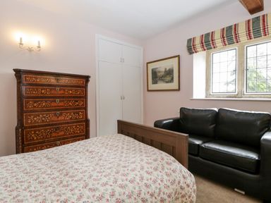 A bedroom with a floral bedspread wooden dresser black leather sofa window with striped curtains and framed artwork at Ham cottage East Lambrook near South Petherton