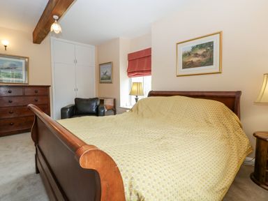A bedroom with a wooden bed and yellow bedspread a black armchair wooden dresser and framed pictures on the walls at Ham cottage East Lambrook near South Petherton