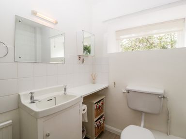 A bathroom with a sink, a mirror, toilet, window with blinds, and storage baskets at Ham cottage in East Lambrook near South Petherton