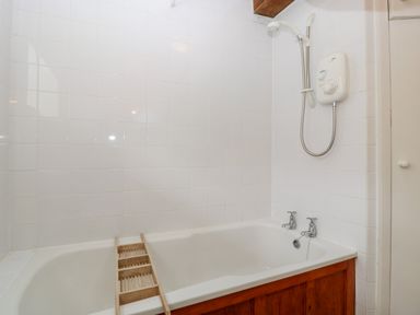 A bathtub with wooden paneling and a mounted shower unit in a tiled bathroom at Ham cottage East Lambrook near South Petherton