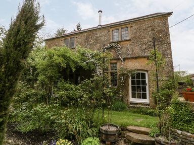 A stone house with vines and plants growing on the facade and garden at Ham cottage in East Lambrook near South Petherton