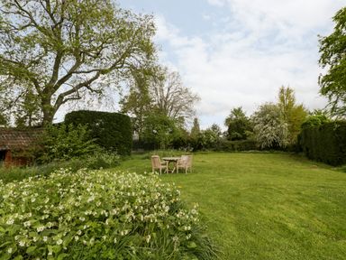 A garden with grass lawn and wooden table with three chairs surrounded by trees and bushes at Ham cottage in East Lambrook near South Petherton