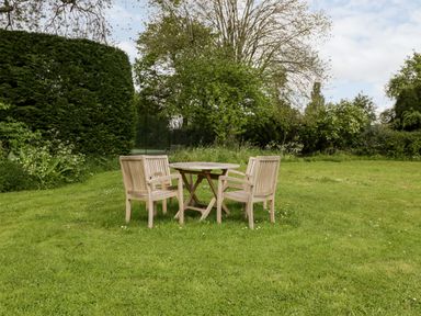 A garden with a round wooden table and four wooden chairs on grass at Ham cottage in East Lambrook near South Petherton