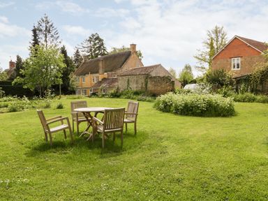 A garden with wooden table and chairs on grass near houses and trees at Ham cottage in East Lambrook near South Petherton