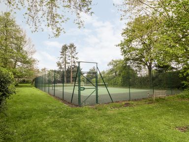 A tennis court surrounded by green fencing with trees and grass around at Ham cottage in East Lambrook near South Petherton