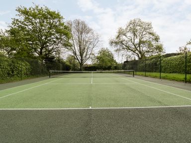 A tennis court with a net surrounded by trees and a green fence at Ham cottage in East Lambrook near South Petherton