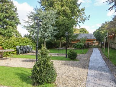 A garden with gravel paths lamp posts bushes stacked chairs and a wooden shed at Pheasant in Bedale