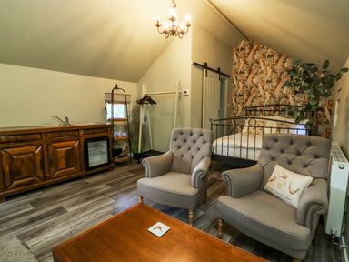 A room with two armchairs a wooden coffee table a double bed with patterned wallpaper behind it a wooden cabinet with a sink and mini fridge and a clothing rack at Pheasant in Bedale