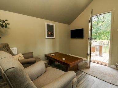A living room with a sofa armchair coffee table TV and an open door leading to a balcony at Pheasant in Bedale