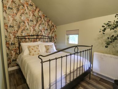 A bedroom with a metal bed frame white bedding birds wallpaper on one wall and a small window by Pheasant in Bedale