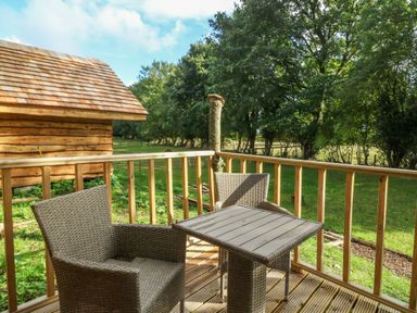 A wooden deck with two wicker chairs and a table overlooking a grassy yard and wooden shed at Pheasant in Bedale