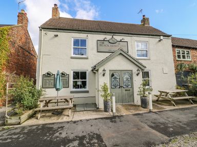 The exterior of The Black Horse Inn with two picnic tables and potted plants at the entrance at Pheasant in Bedale