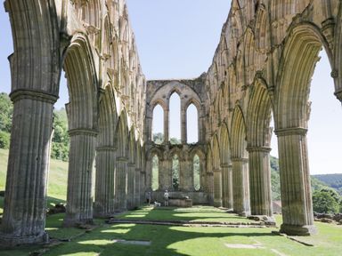 Stone arches and columns of a historic abbey ruin with grassy floor and people walking at Pheasant in Bedale