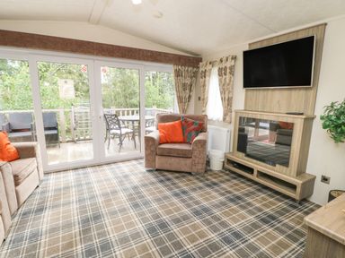 A living room with armchairs a wall mounted tv and glass doors leading to a deck with outdoor furniture at Bock Retreat in Felton